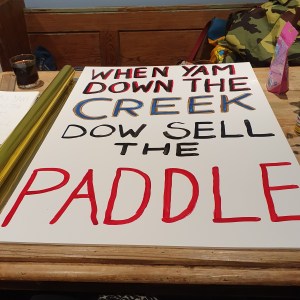A partially painted placard reading "When yam down the creek dow sell the paddle"
