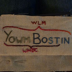 "Yowm Bostin" embroidered in multicoloured thread on tabby weave linen, with a parenthesis over "Yowm Bostin" pointing to the letters WLM and a parenthesis under "Yowm Bost" pointing to the letters WMBC