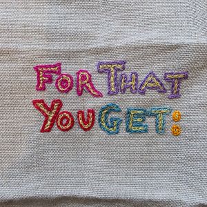 "For That You Get" embroidered in multicoloured thread on tabby weave linen