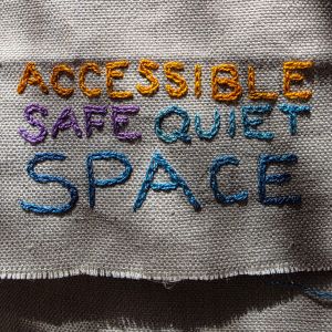 "Accessible safe quiet space" embroidered in multicoloured thread on tabby weave linen