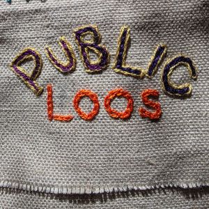 "Public Loos" embroidered in multicoloured thread on tabby weave linen